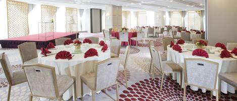Un salón de banquetes con mesas redondas, sillas y un escenario.
