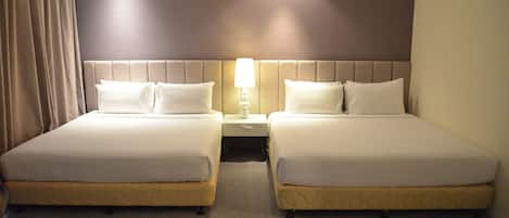 A hotel room with two beds, a nightstand with a lamp, and a curtain.