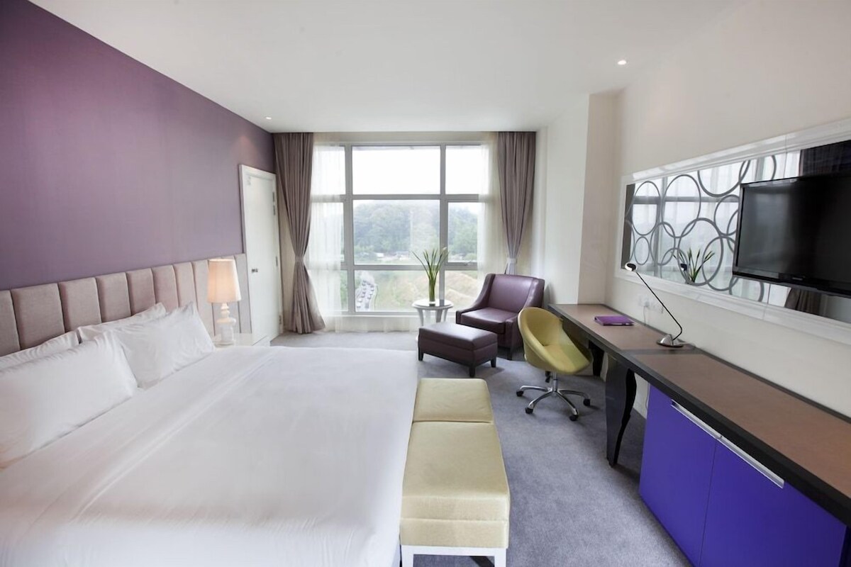 A hotel room with a large bed, a desk with a computer, a chair, and a television.