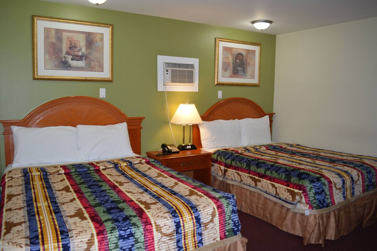 A hotel room with two beds, a nightstand with a lamp, and framed artwork on the walls.