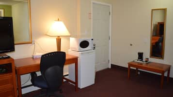A hotel room with a desk, chair, microwave, lamp, and a small table with a coffee maker.