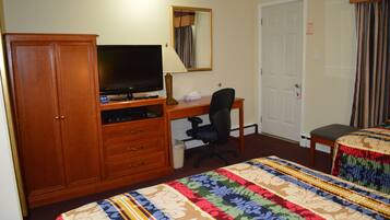 Habitación de hotel con un armario de madera, un escritorio con computadora y televisor de pantalla plana, una cama individual con colcha estampada y una puerta con espejo arriba.
