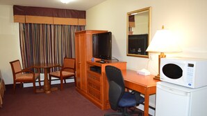 Une chambre d’hôtel équipée d’un bureau en bois, d’une télévision, d’un four à micro-ondes, d’une chaise et d’une petite table.