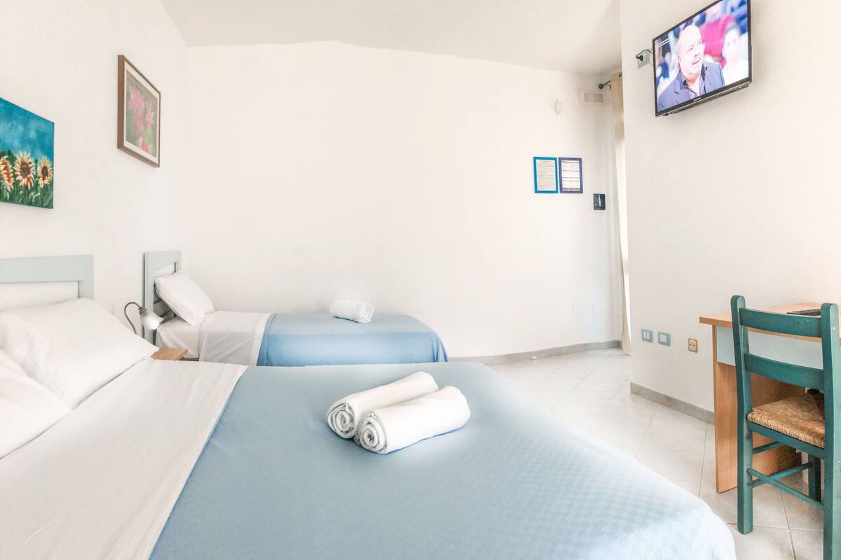Une chambre d’hôtel avec deux lits, un bureau, une chaise, une télévision et un tableau au mur.