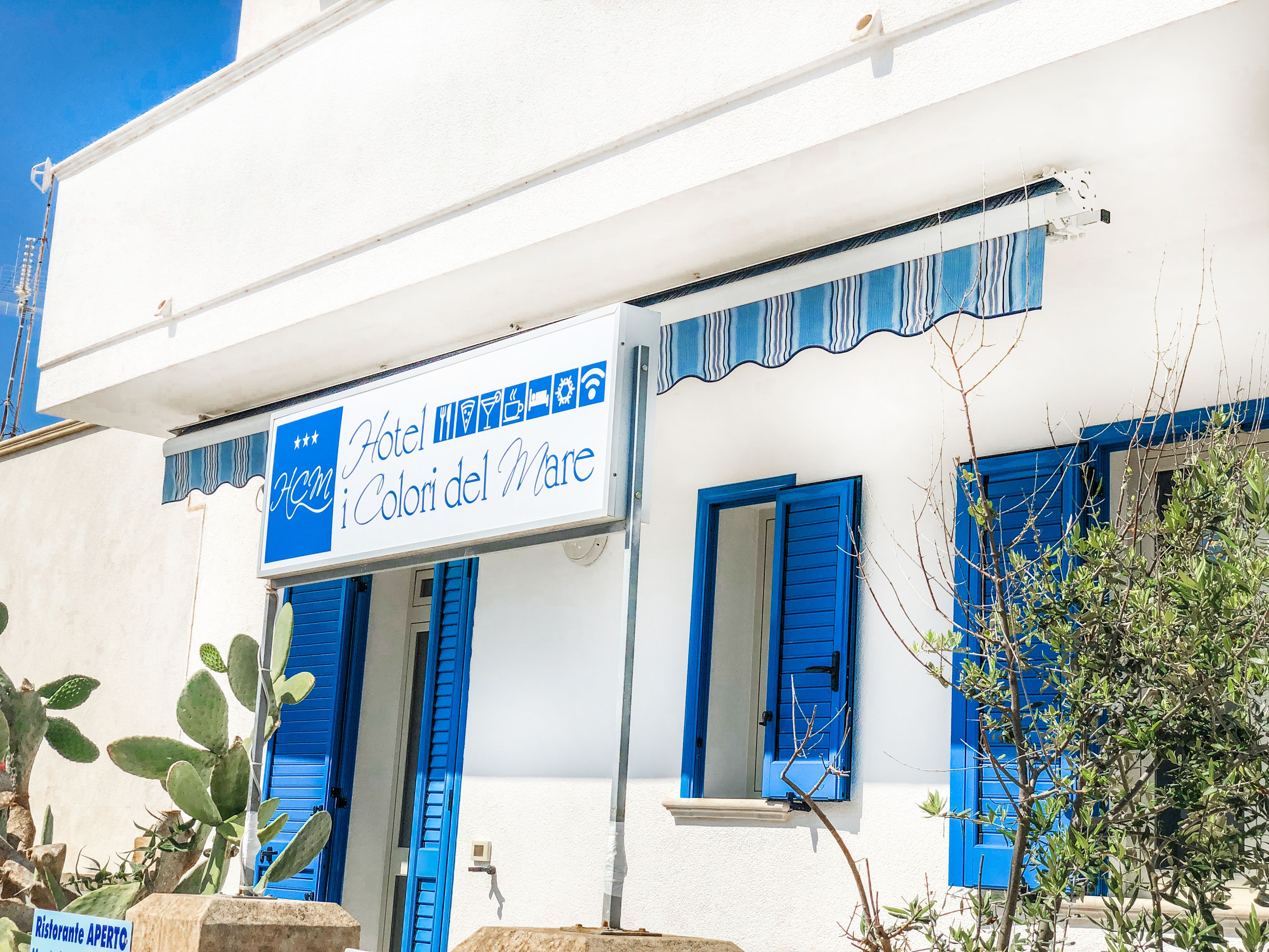 A hotel named "Hotel iColori del Mare" with blue shutters and a white facade.