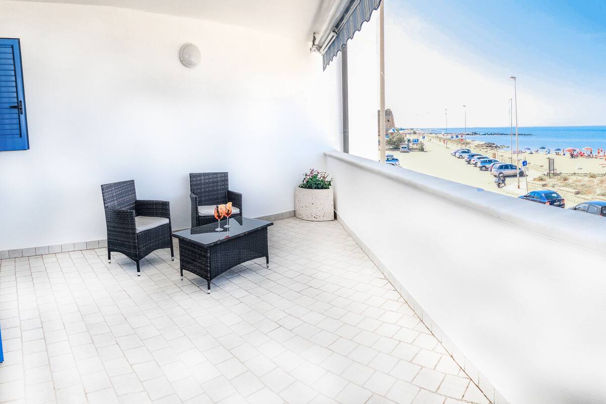 Un balcon donnant sur une plage, une table avec un verre et deux chaises.