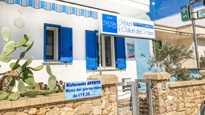 Un edificio blanco con contraventanas azules y un letrero que dice "Hotel Distanza dei Colori del Mare".