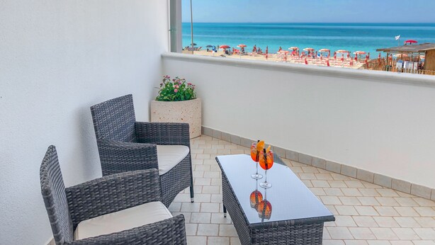 Un balcón con mobiliario de mimbre, una pequeña mesa con bebidas y vistas a la playa.
