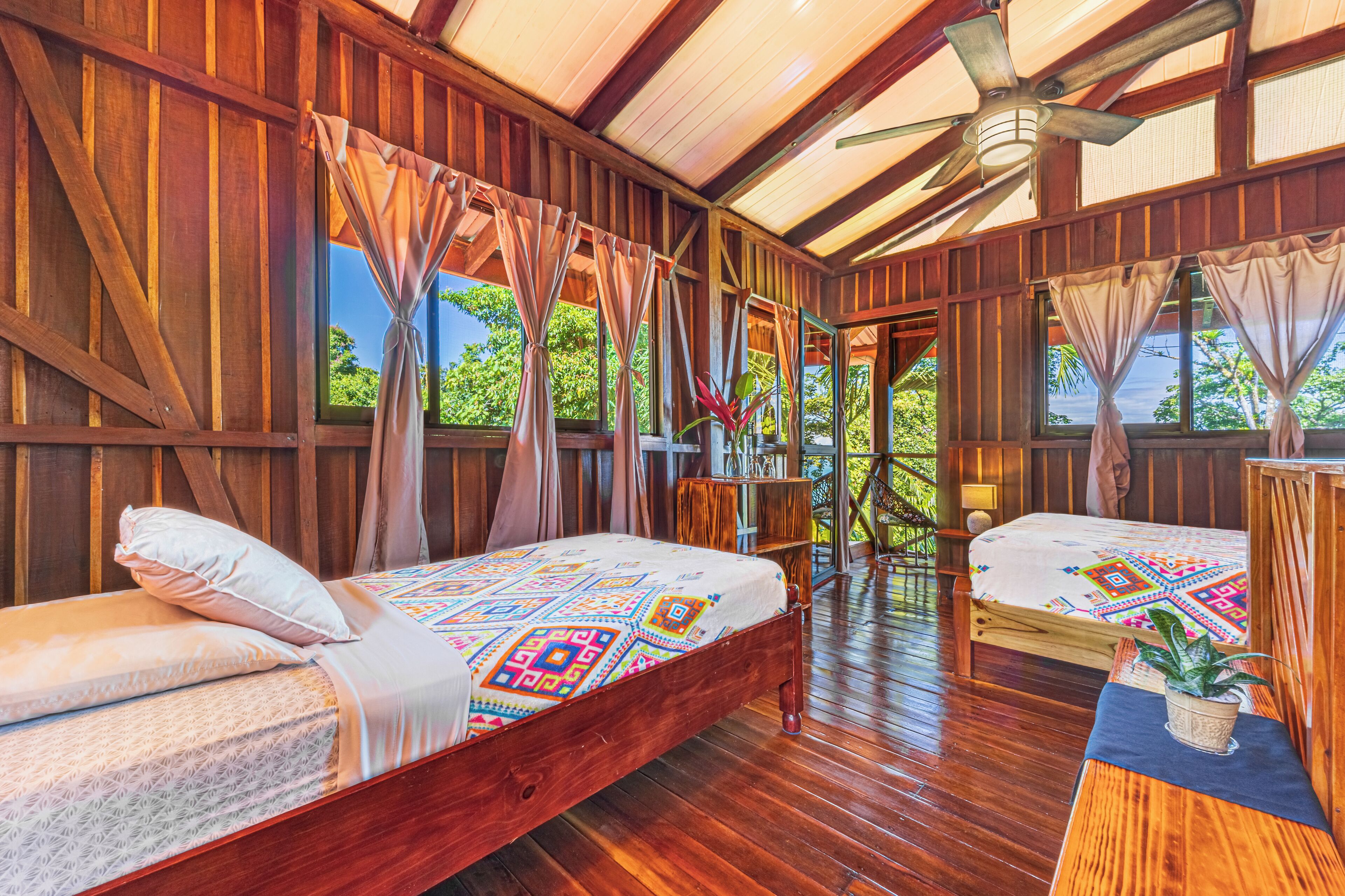 A wooden room with two beds, a ceiling fan, and large windows.