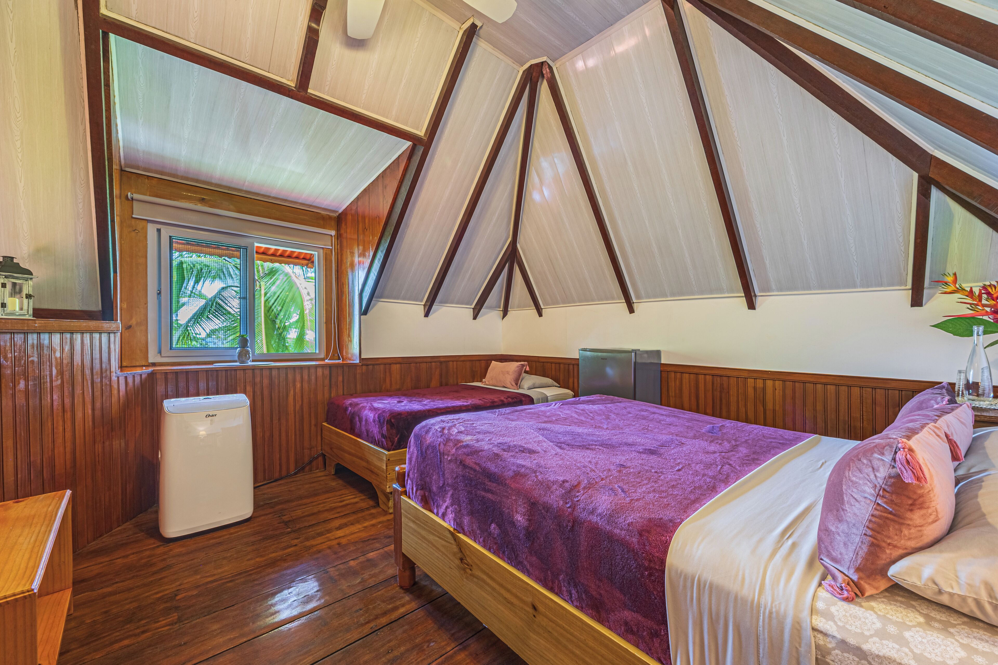 Ein Zimmer mit zwei Betten, Holzboden, einem kleinen Heizgerät, einem Fenster mit Blick und einer Decke mit Holzbalken.