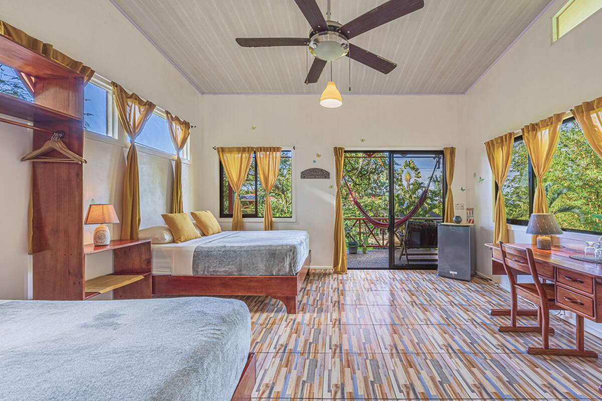 A room with a bed, a desk, a chair, a ceiling fan, and a view of the outdoors.