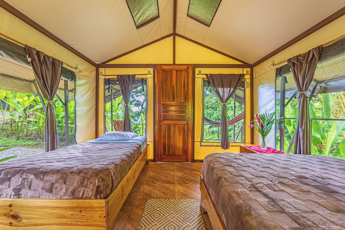 A cozy room with two wooden beds, a wooden door, and large windows with curtains.