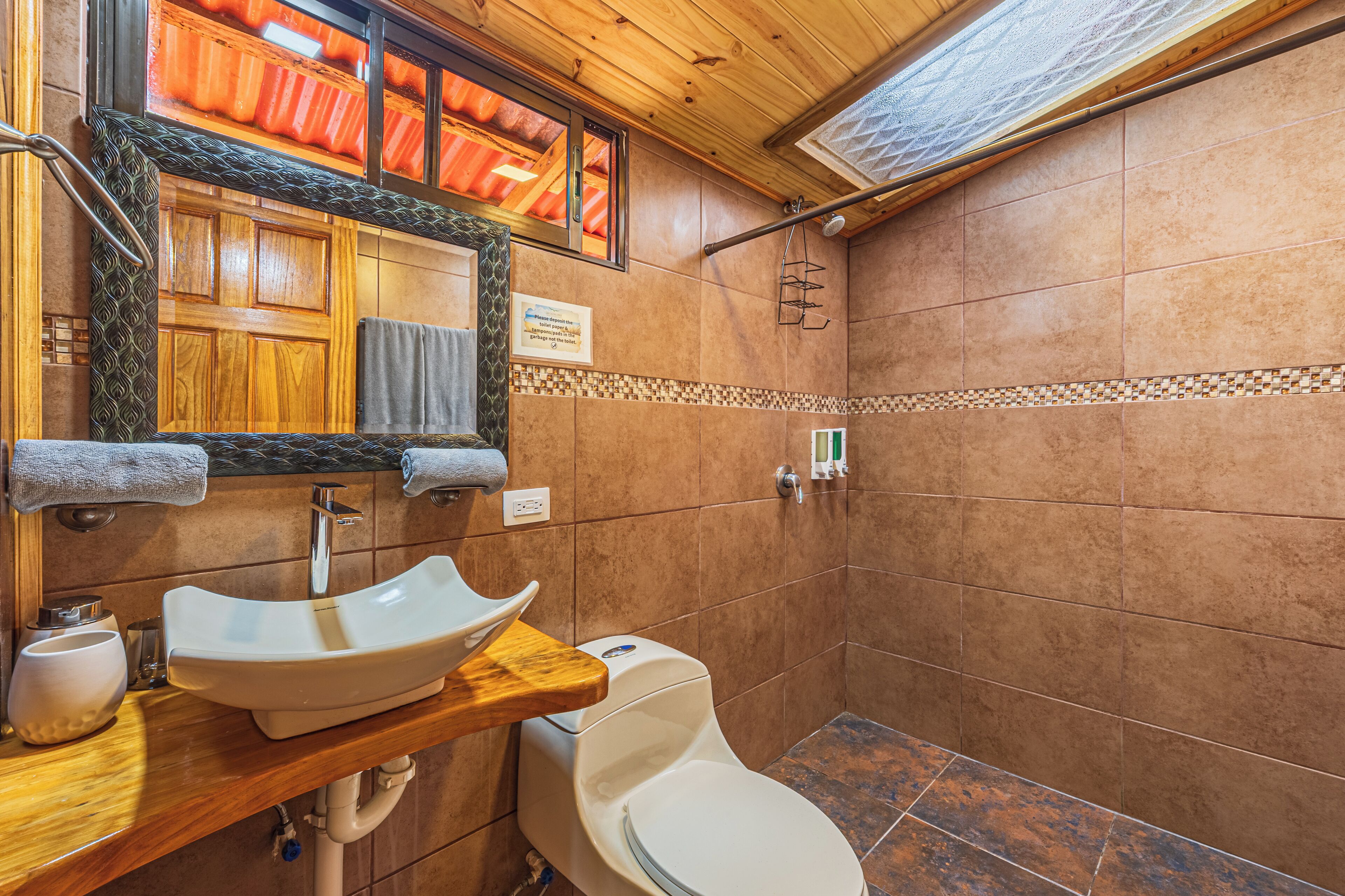 A bathroom with a wooden vanity, a white sink, a toilet, and a shower area.