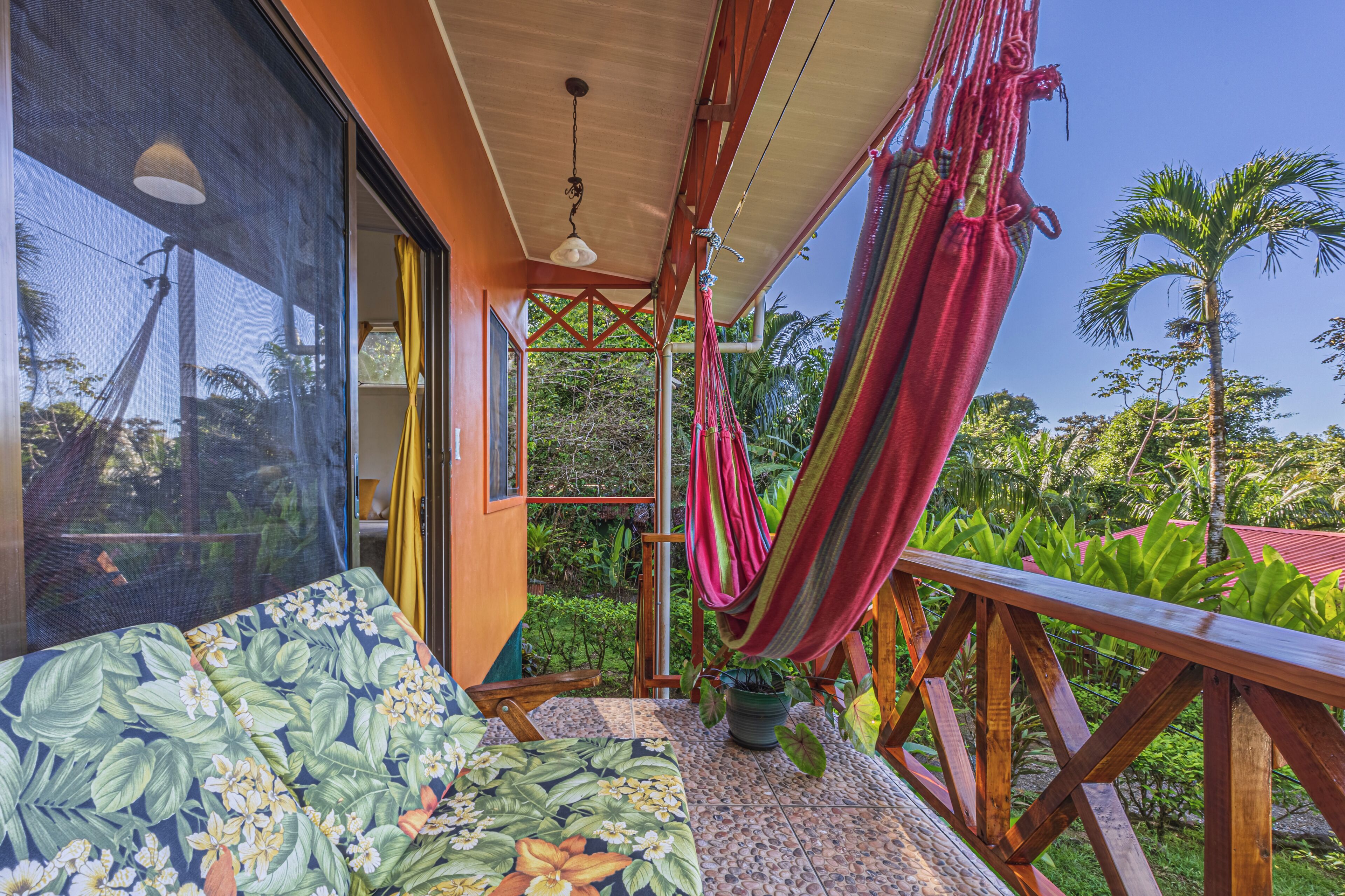 A room with a bed, a hammock, and a view of lush greenery.