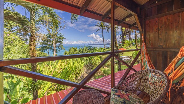 Una estructura de madera con vistas a un paisaje tropical, que incluye palmeras y una playa.