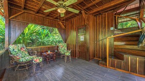 Interior de madera con una escalera, sillas de mimbre y vistas a exuberante vegetación.