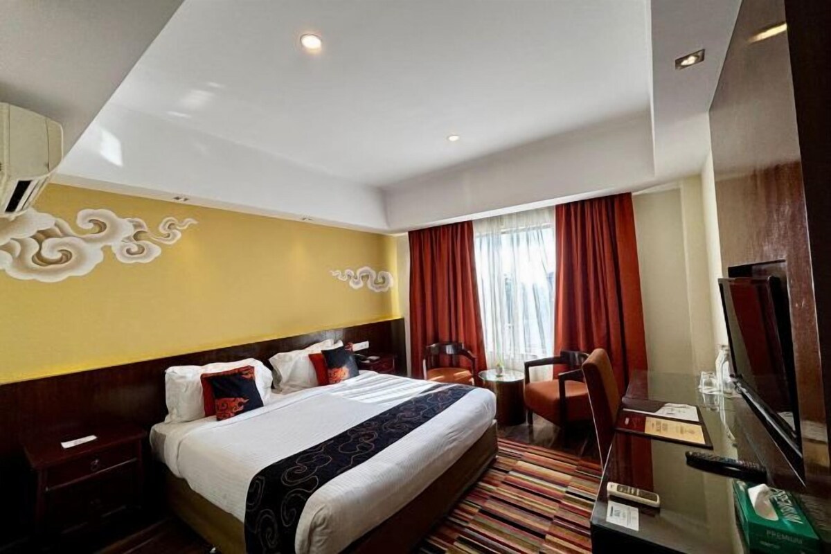 Habitación de hotel con cama, escritorio, silla, televisor y ventana con cortinas.