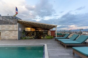Un área de piscina en la azotea con sillones de descanso, un bar y vistas a la ciudad.