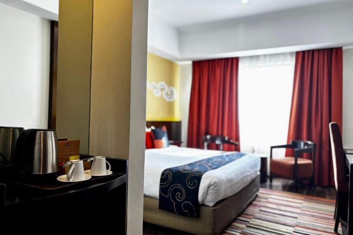 Ett hotellrum med en säng, ett skrivbord med en kaffebryggare och en stol.