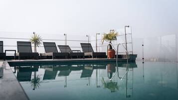Vista clara de uma piscina com espreguiçadeiras e um grande vaso de plantas.