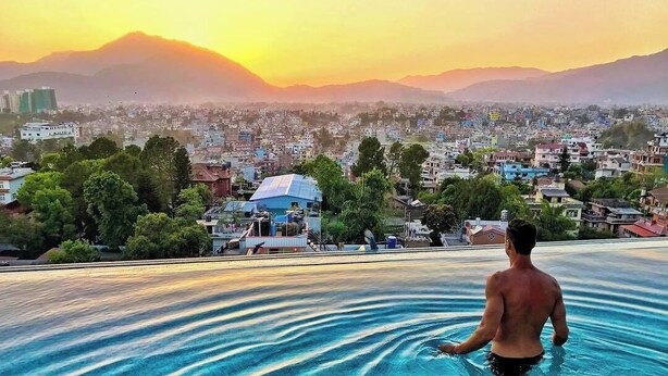 A man in a swimming pool overlooking a cityscape with mountains in the background. - Hotel Shambala (Kathmandu)