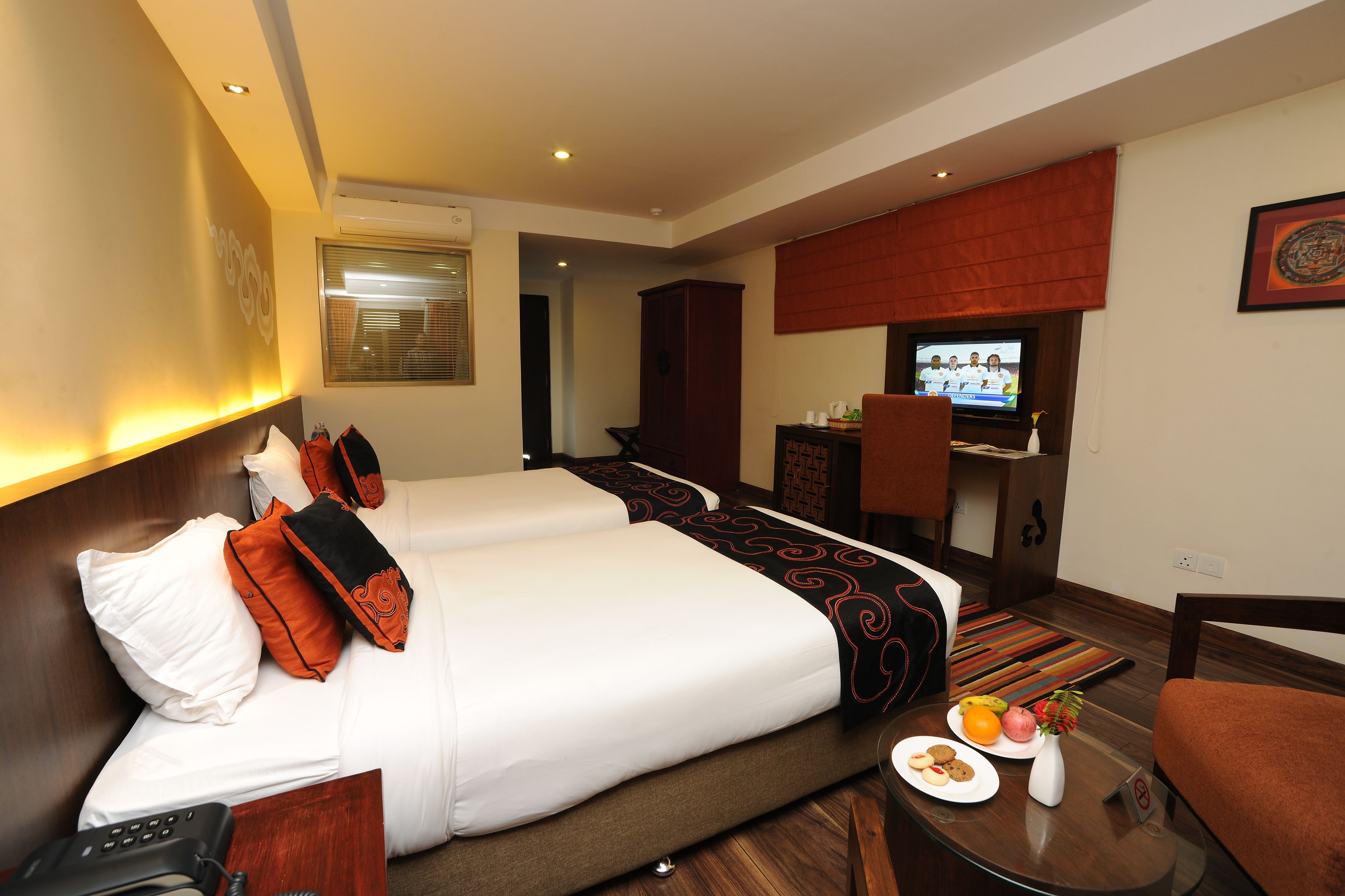 Een hotelkamer met twee bedden, een televisie, een eettafel met eten en drinken, en een klein kastje.
