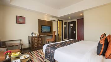 Habitación de hotel con cama, escritorio, silla, televisor y un pequeño rincón de comedor con un frutero.