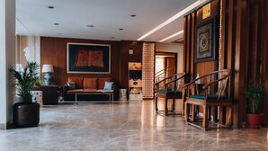 A spacious lobby with a marble floor, a sofa, a wooden chair, a lamp, and a potted plant. - Hotel Shambala (Kathmandu)