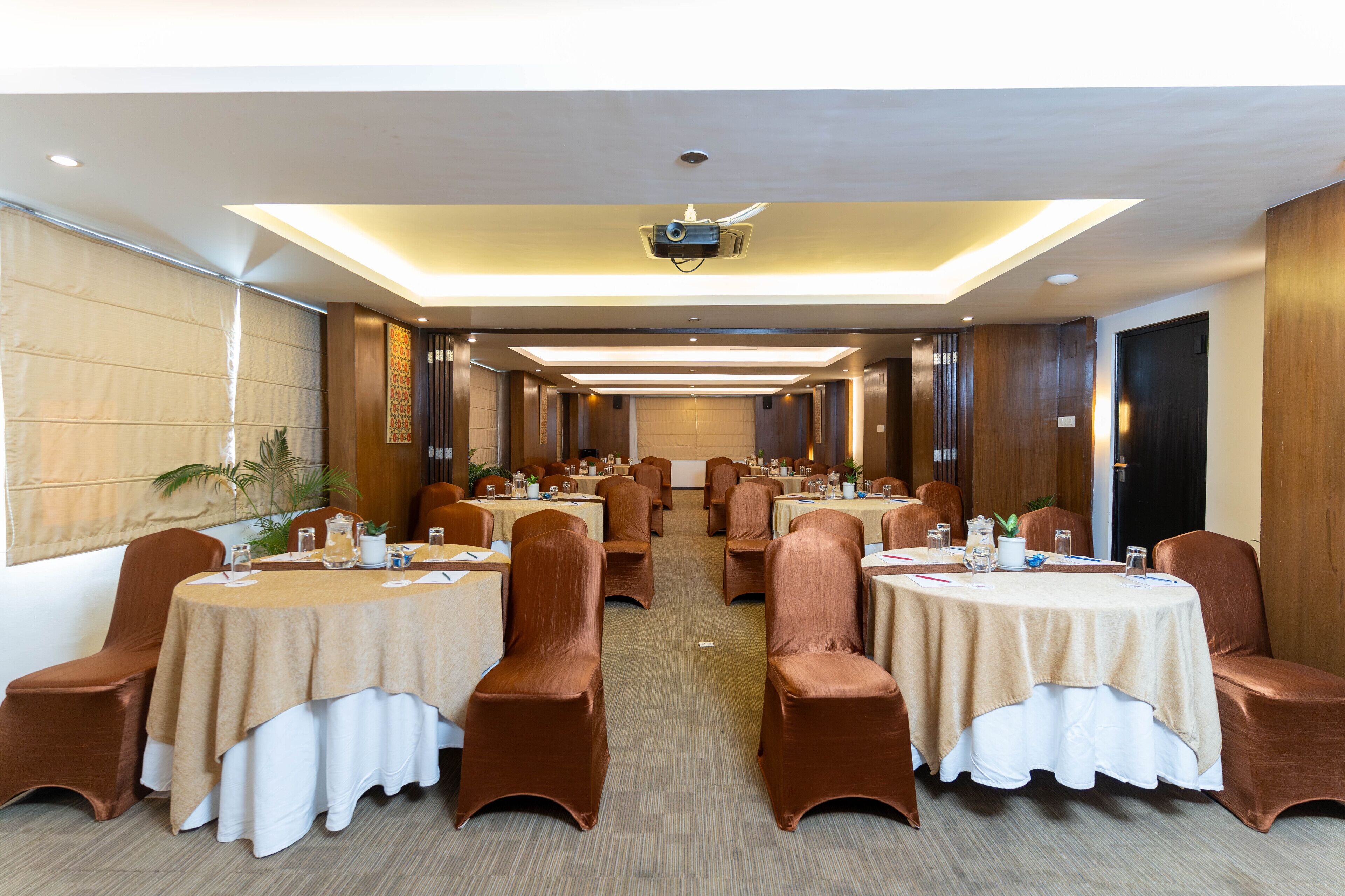 A conference room with round tables, brown chairs, and beige tablecloths.