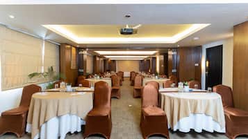 A conference room with round tables, brown chairs, and beige tablecloths.