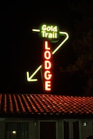 Letrero de neón que indica 'Gold Trail Lodge' con flechas direccionales.