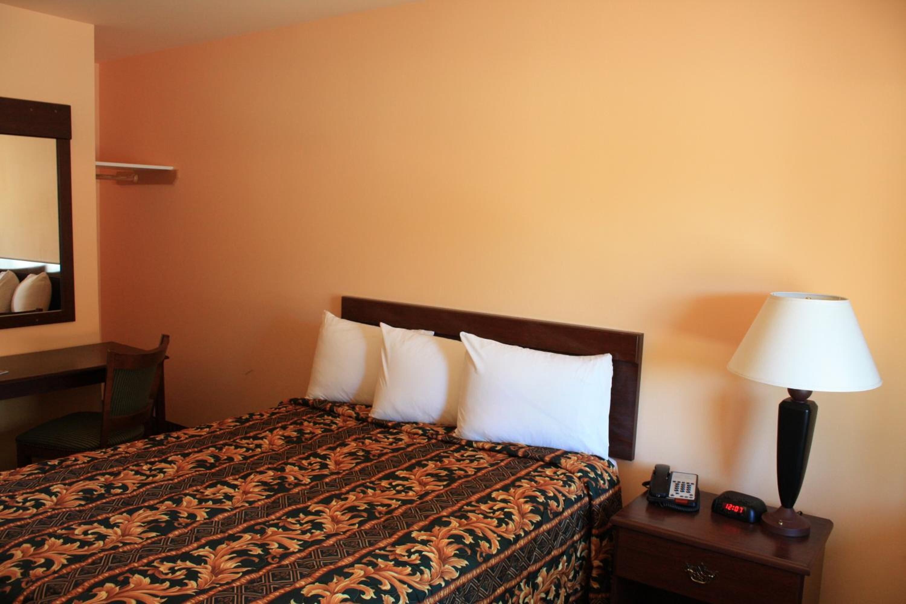 A hotel room with a bed, a bedside table with a lamp, a phone, and a mirror on the wall.