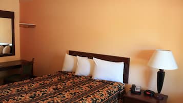 A hotel room with a bed, a bedside table with a lamp, a phone, and a mirror on the wall.