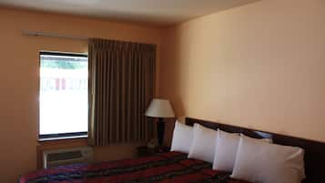 Habitación de hotel con cama, ventana con cortinas, equipo de aire acondicionado y mesita de noche con lámpara.