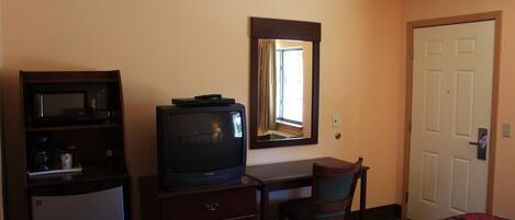 Una habitación de hotel con una cama, un televisor en una cómoda, un escritorio con una silla y una puerta.