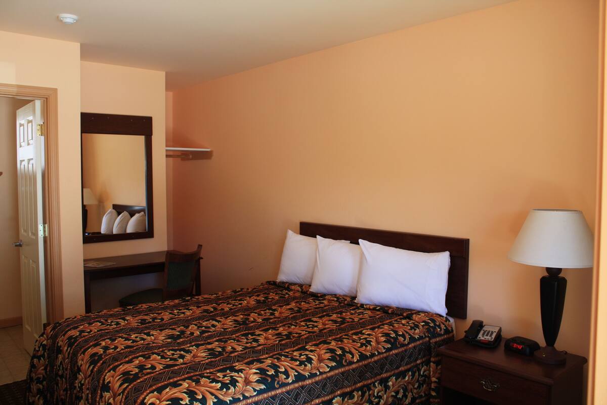 A hotel room with a bed, bedside table, lamp, and a mirror on the wall.