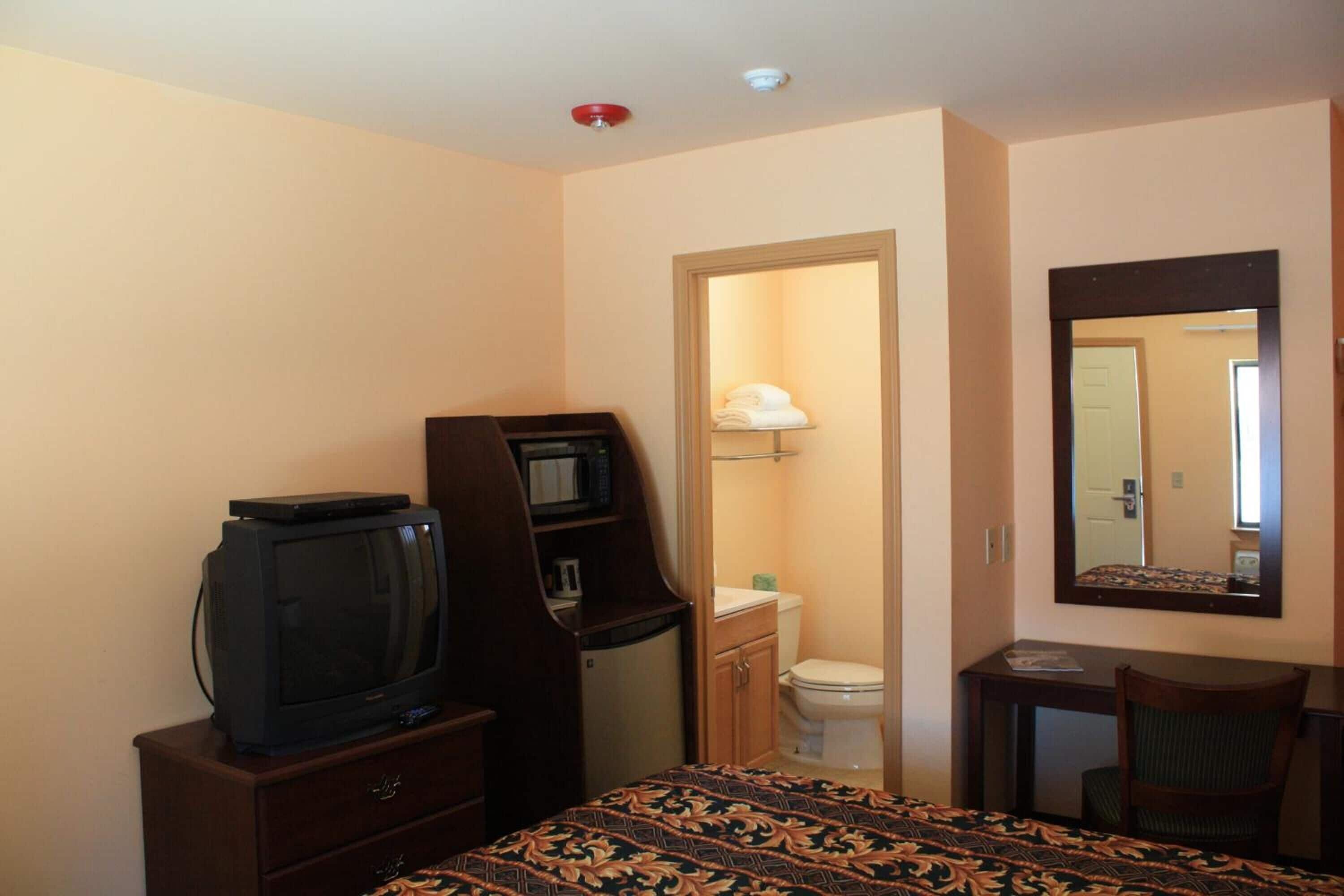A hotel room with a bed, a television, a desk, a chair, a mirror, and a bathroom.