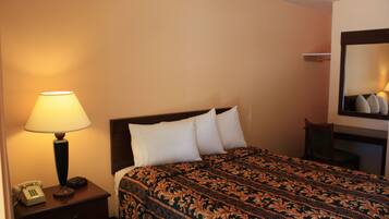 Habitación de hotel con cama, mesita de noche con lámpara y teléfono, y espejo en la pared.