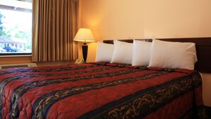 Ein Hotelzimmer mit einem großen Bett, einem Fenster mit Vorhängen, einer Nachttischlampe und einem Telefon auf dem Nachttisch.