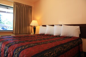 Una habitación de hotel con una cama grande, una ventana con cortinas, una lámpara de noche y un teléfono en la mesita de noche.
