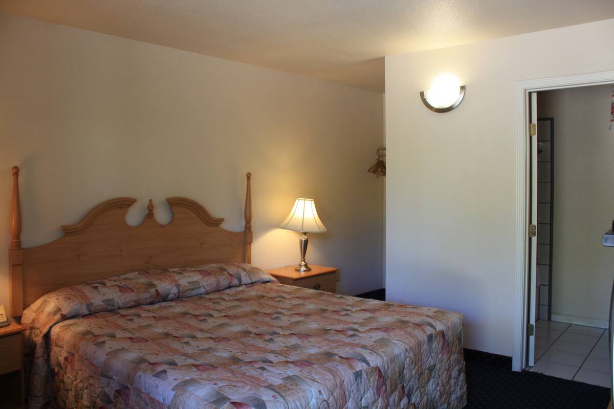 A hotel room with a wooden headboard bed, a bedside lamp, and a door leading to another room.