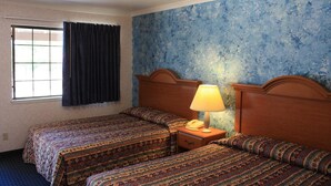 A hotel room with two beds, a window with curtains, a nightstand with a lamp, and a textured blue wall. - Mother Lode Motel (Placerville)