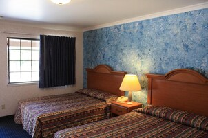 Habitación de hotel con dos camas, una ventana con cortinas, una mesita de noche con lámpara y una pared azul con textura.