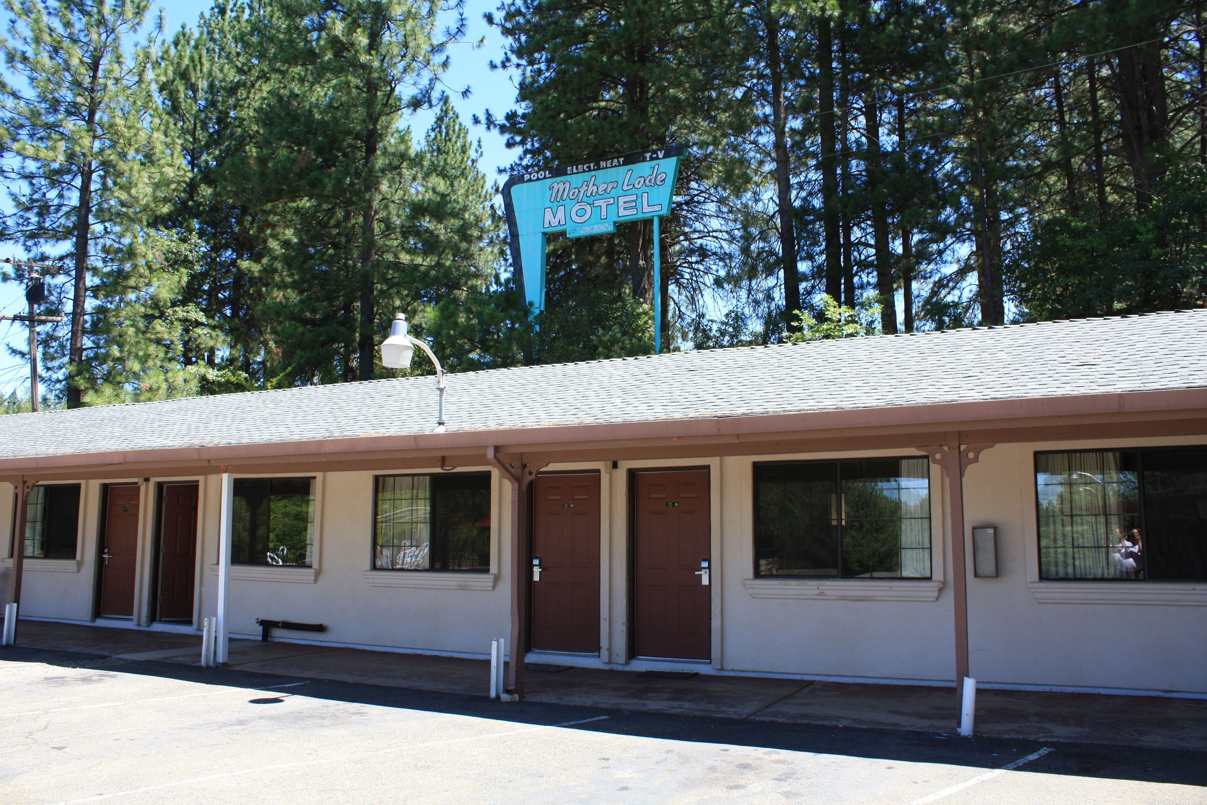 A motel with a signboard, multiple doors, windows, and a parking lot.