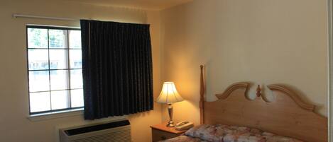 A hotel room with a bed, a nightstand, a lamp, a telephone, and a window with curtains.