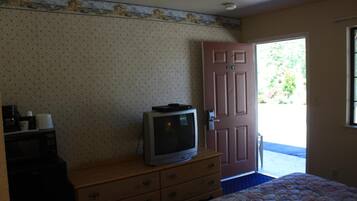 Un dormitorio con cama, cómoda, televisor y puerta que da al exterior.