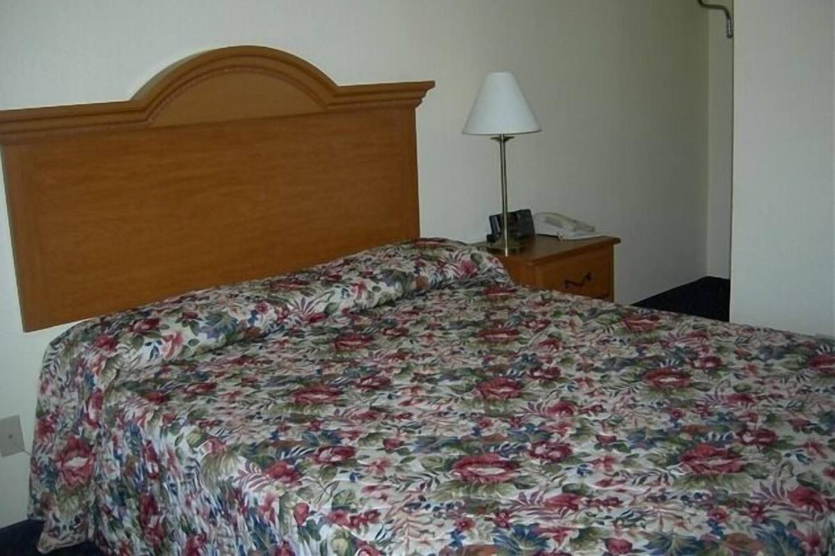 A bed with a floral bedspread, a wooden headboard, a bedside lamp, and a small bedside table with a phone.