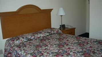Una cama con una colcha estampada, un cabecero de madera, una lámpara de noche y una mesita de noche con un teléfono.