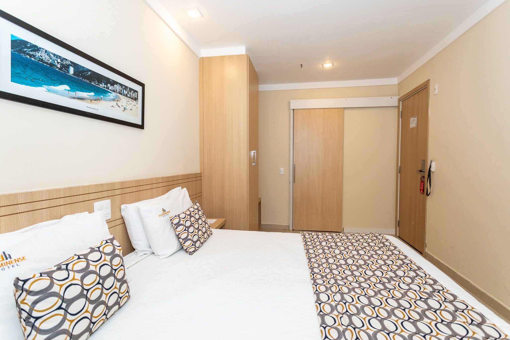 Une chambre d’hôtel avec un lit, une table de chevet, un tableau encadré au mur et une porte.