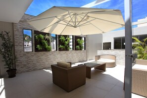 A modern outdoor patio with wicker furniture, a large umbrella, and potted plants. - Fluminense Hotel (Rio de Janeiro)